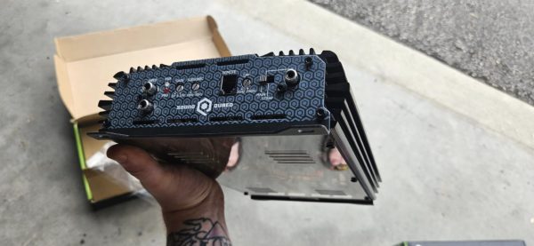 A person holding up a small black box containing a Soundqubed S1-1250 Monoblock Amplifier.