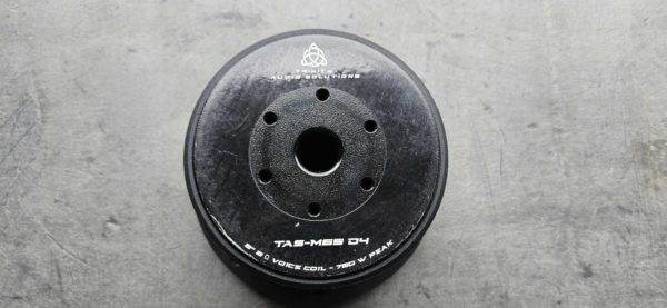 BSTOCK - Trinity Audio Solutions TAS-M65 D2, a black disc with holes on it on a concrete surface.