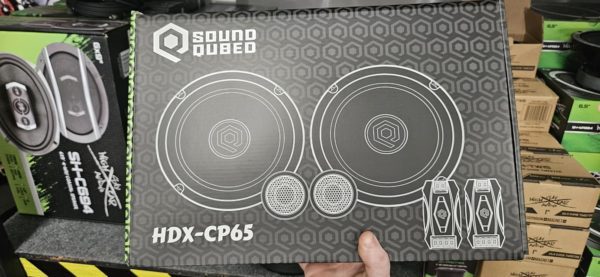 A person is holding a box of Soundqubed HDX Series 6.5" Component Set speakers in a store.
