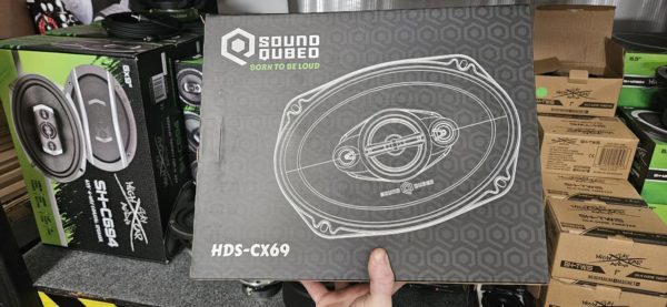 A person is holding up a box of Soundqubed HDS Series 6x9" inch 3-way Coaxial Speaker (Pair) in a store.