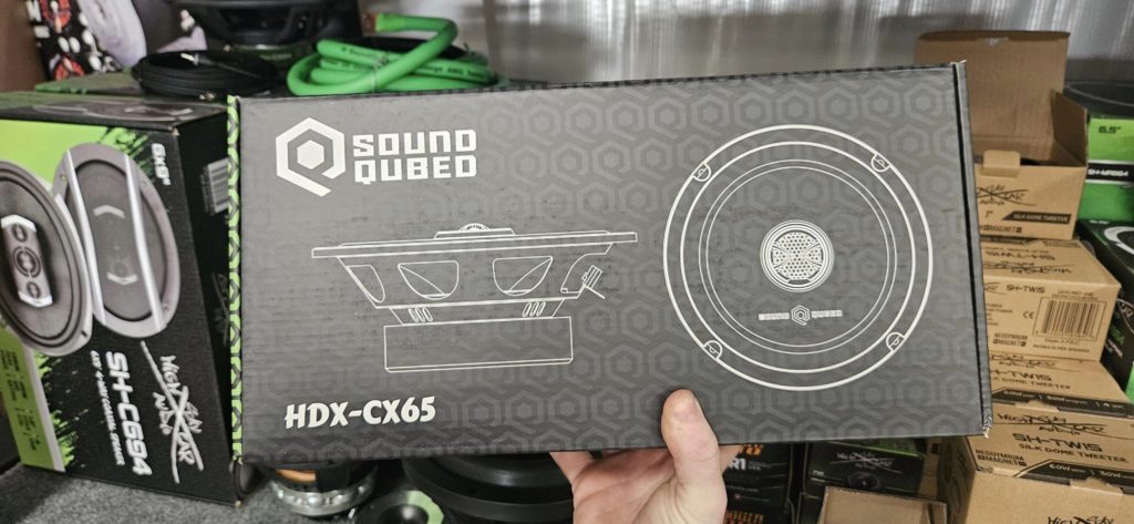 A person is holding up a box of Soundqubed HDX Series 6.5" Coaxial 2-way Speakers (Pair).