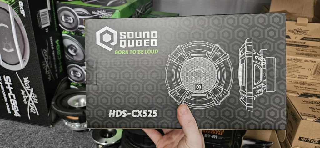 A person is holding up a box of Soundqubed HDS Series 5.25" Coaxial 2-way Speakers (Pair).