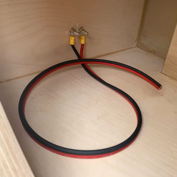 A red wire is connected to an Adire Audio Performance Series – Dual 10″ 2.5 Cf Net Ported Enclosure.